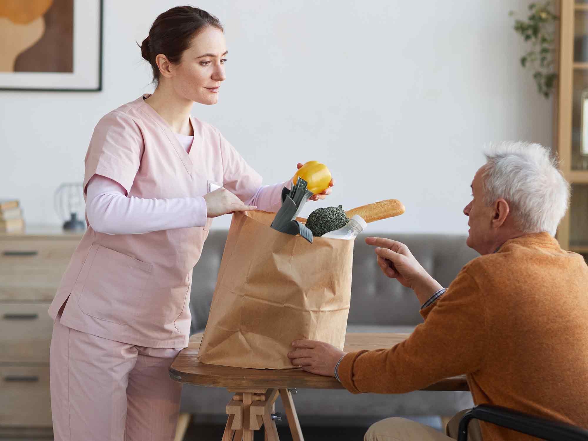 Altenpflegerin übergibt Einkaufstüte an alten Mann