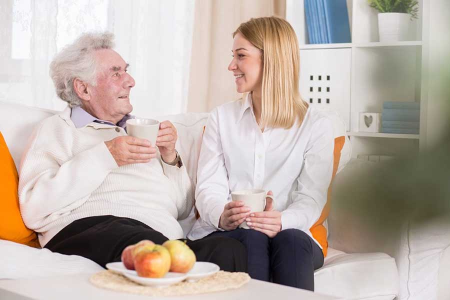 Junge Frau sitzt neben Rentner der eine Tasse in der Hand hält